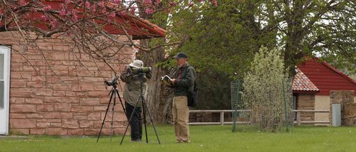 2 people on Malheur NWR using telescopes and binoculars, bird watching near 2 building scenic trees and bushes
