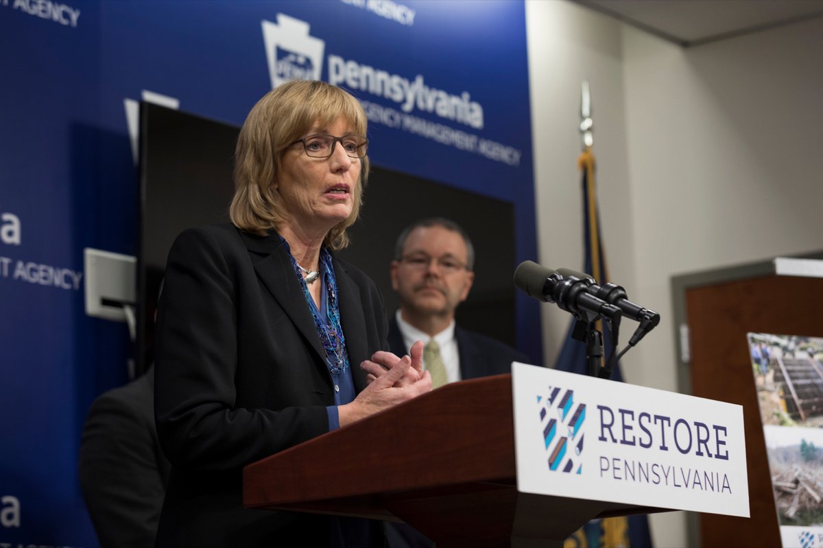 DCNR Secretary Cindy Adams Dunn speaks at podium with microphone and Restore Pennsylvania logo while PEMA Director Randy Padfield stands behind her looking on.