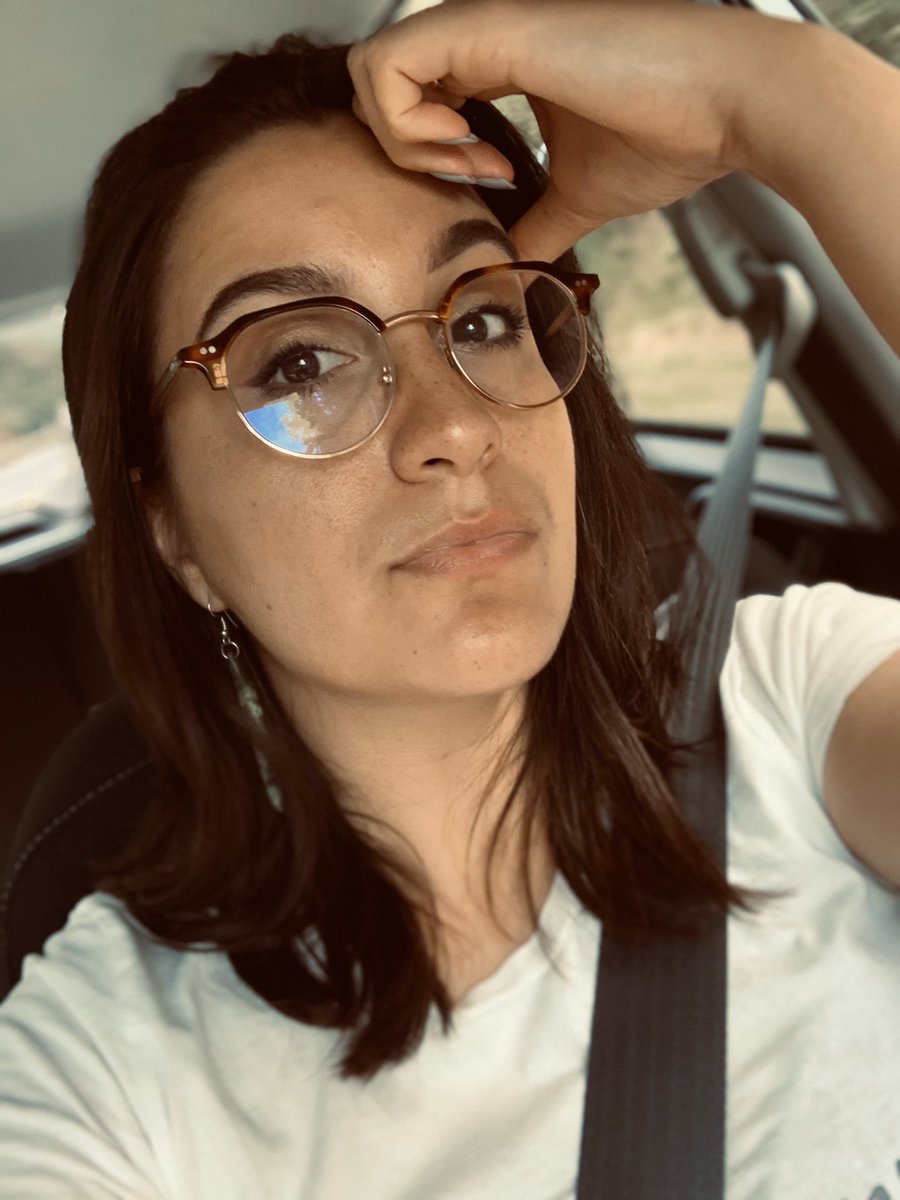 Selfie of Kera in the car - she is wearing glasses, pounamu earrings and a white activist t-shirt. She  looks unimpressed.