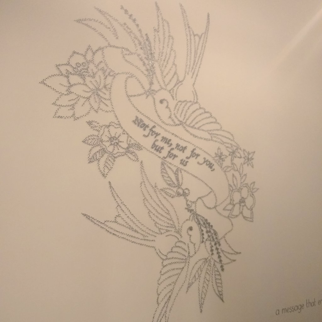 An artwork of two birds on a white wall made of black pins, saying not for me, not for you, but for us