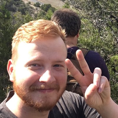profile of Caleb with his hand doing a peace sign. Someone is behind him, looking at the canyon view behind him.