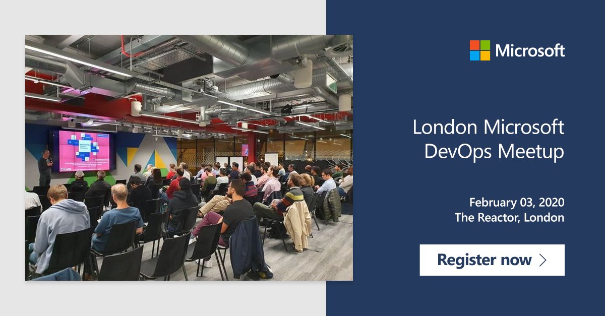 Group of people are sat down at a small event hall, in front of a stage. Their seats are aligned. They are listenting and watching someone present. There is a large screen in front of them.