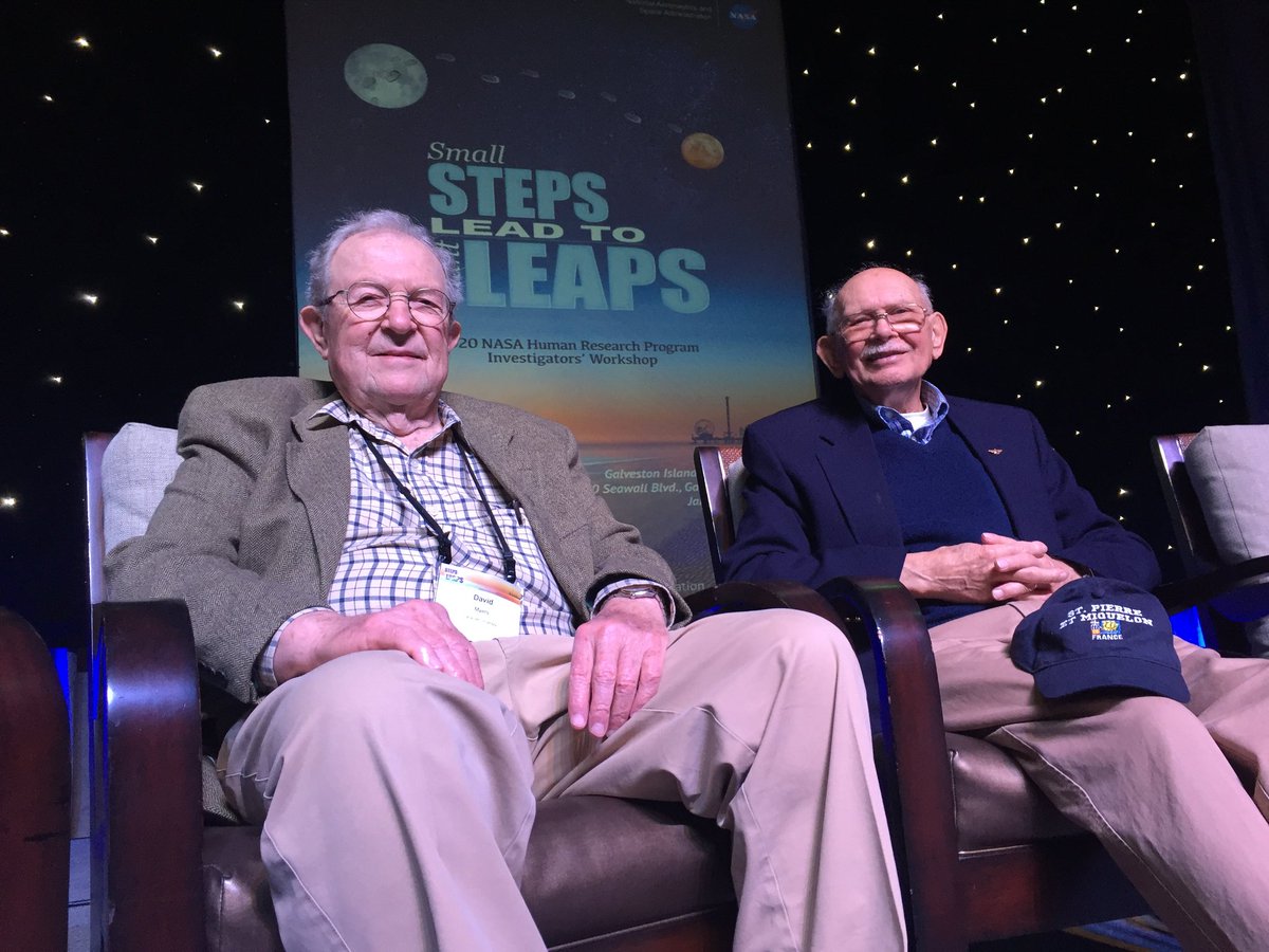 Two white presenting men in their 70s sit in chairs smiling at the camera.