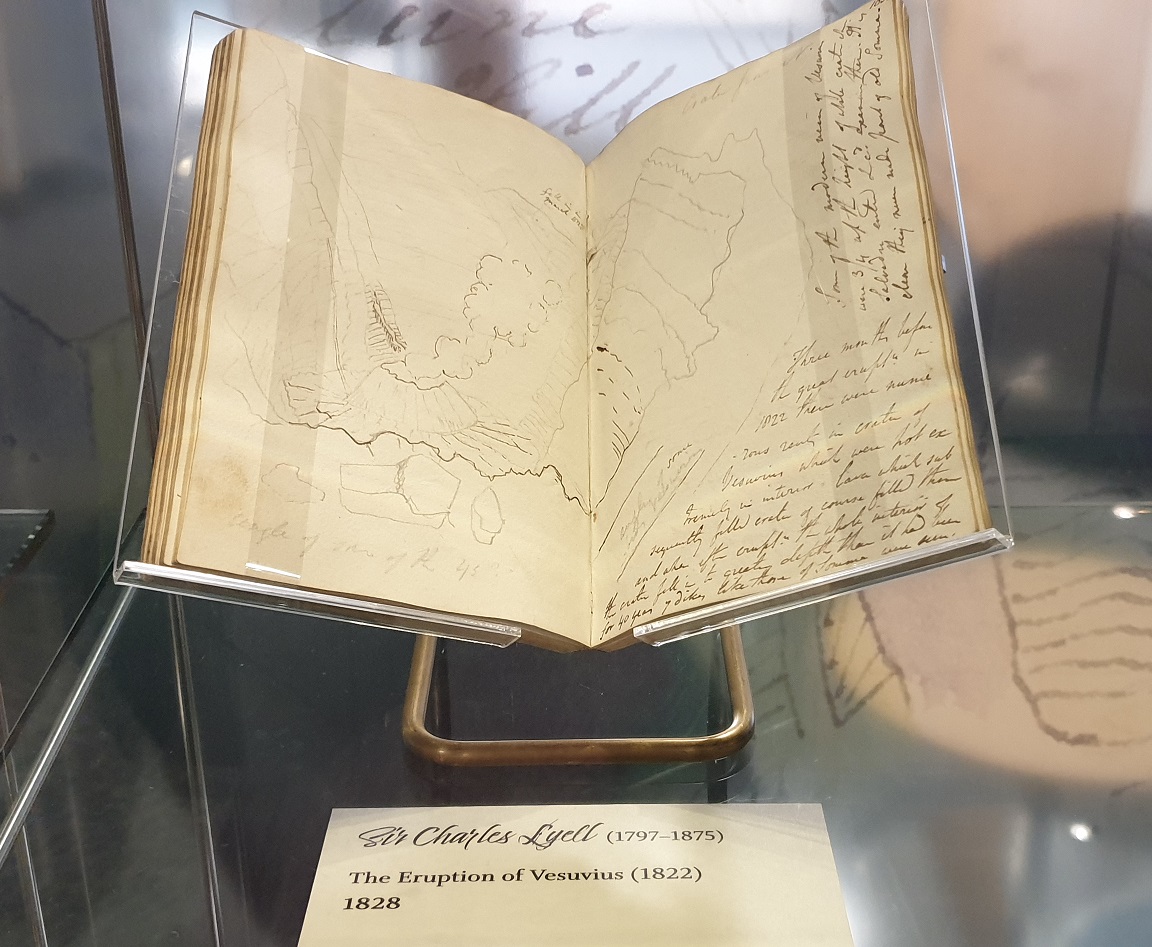 Image is a photo of one of the notebooks on exhibition. This one has a hand drawing of the eruption of Vesuvius in 1822, with handwritten annotations around the side.