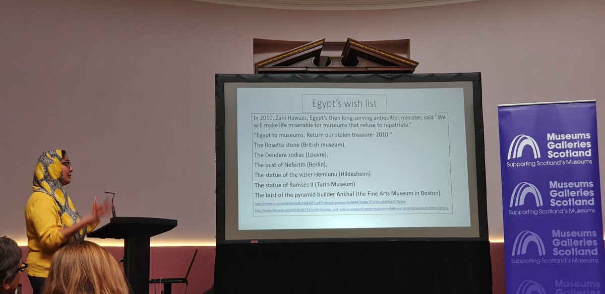 Abeer Eladany speaking by a screen listing famous Egyptian objects taken and displayed in museums in Europe.