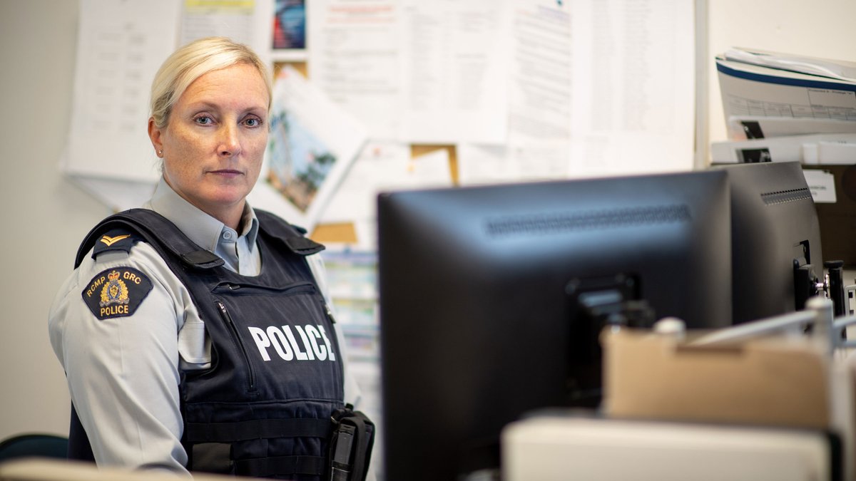 Female police officer sitting at a desk staring into the camera.