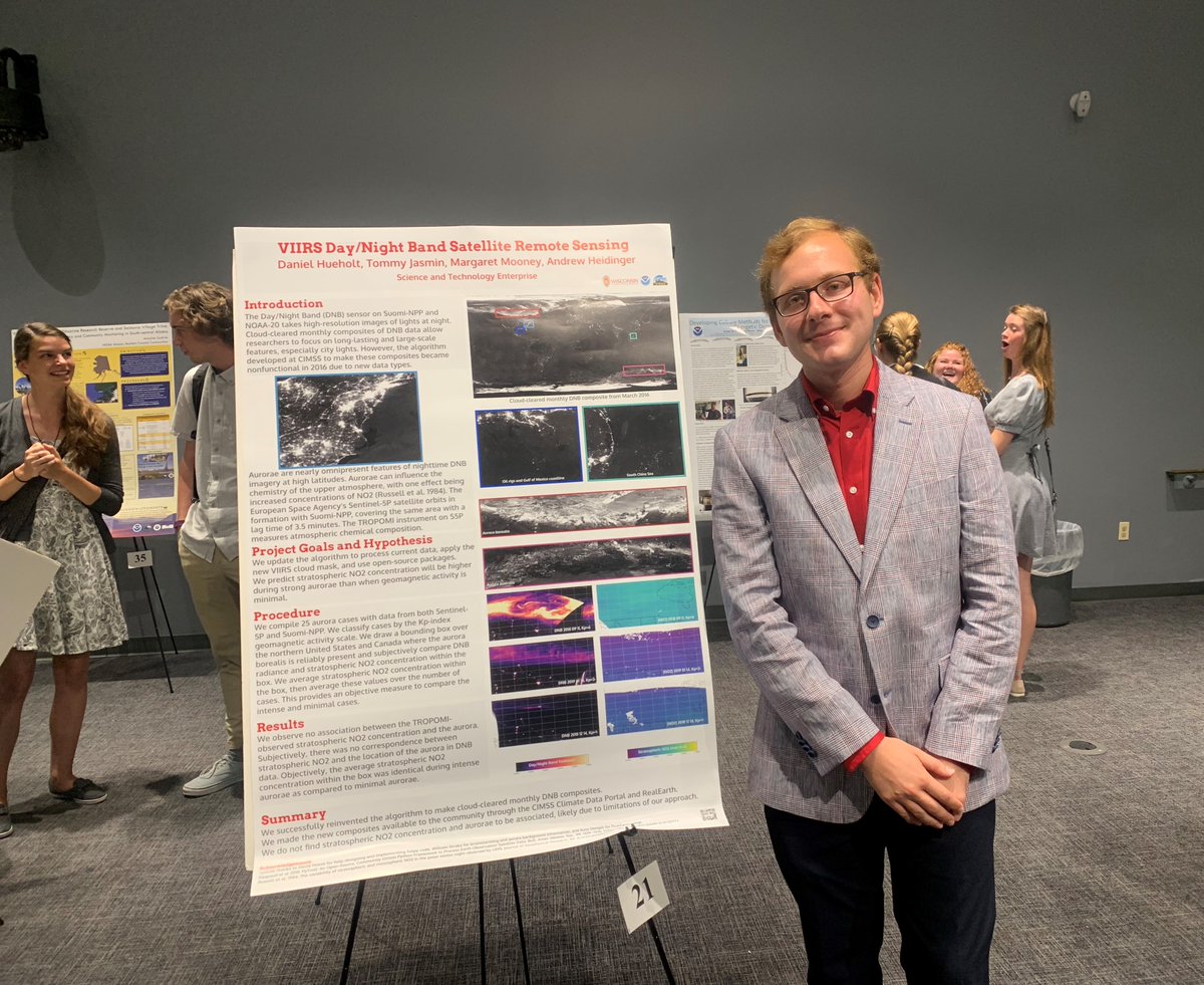 A male student smiles while standing next to his research poster.