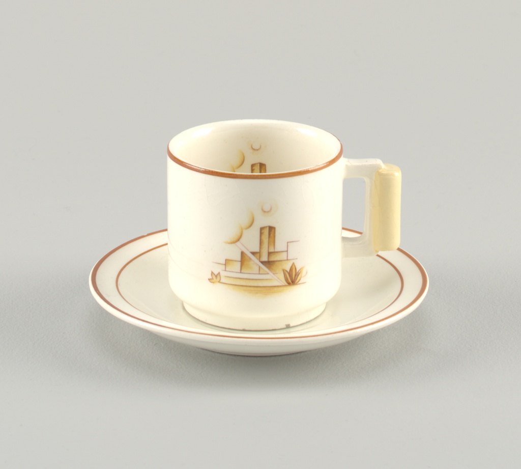 A cream-colored cup and saucer with an abstract depiction of a cityscape printed on it. 