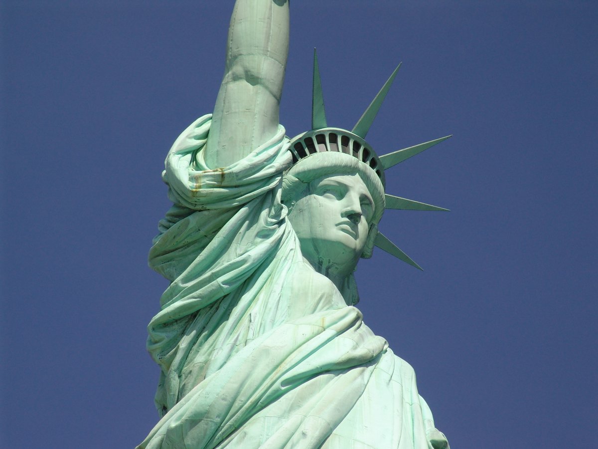 Up close right side view of the Statue of Liberty featuring the lower arm and shoulder with blue sky in background.  