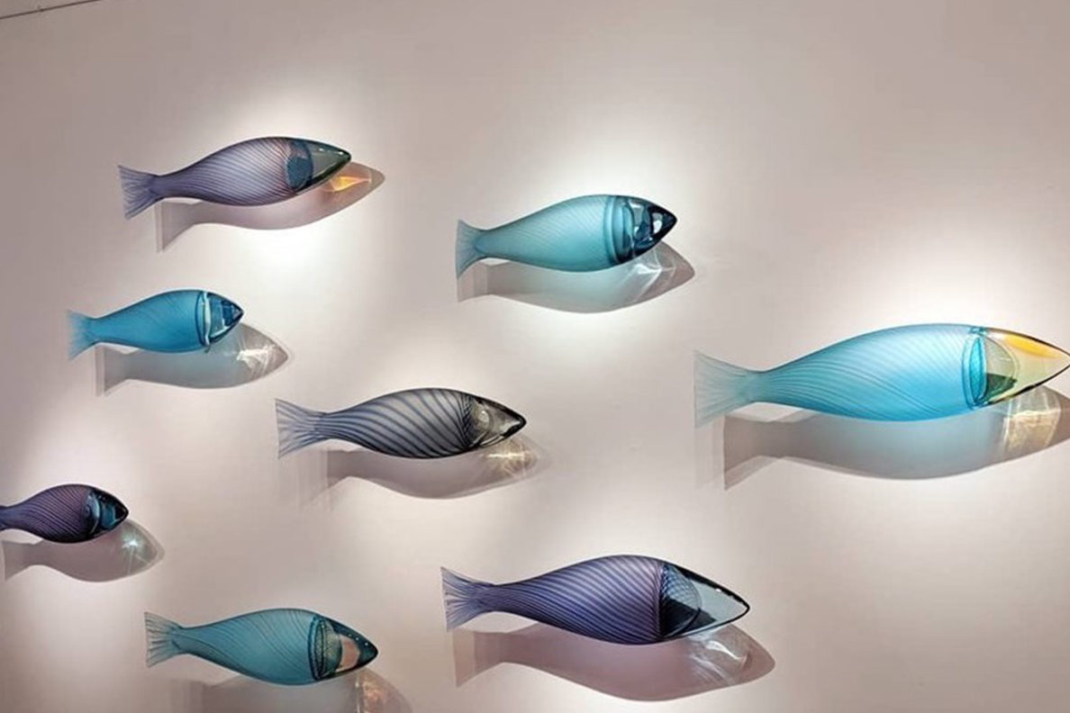 Multi-color glass fish are attached to a library wall. The fish appear to be swimming, with various points of light casting different shadows. 