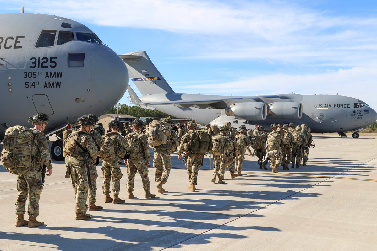 Soldiers walk in a single-file line on the flight line, to board a C-17a military transport aircraft.