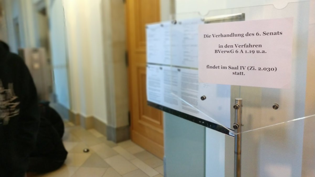 Im Bundesverwaltungsgericht warten ein paar linksunten-Unterstützer vor den Türen von Gerichtssaal römisch vier.