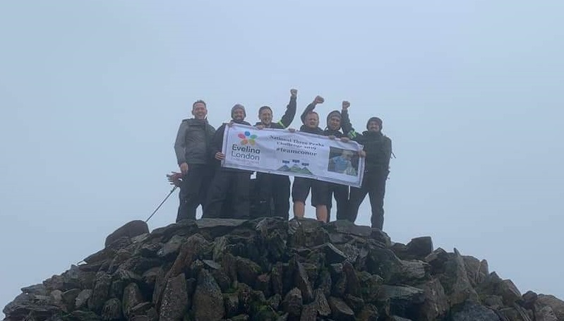 A group of our supporters standing on top of a mountain with an Evelina London sign.