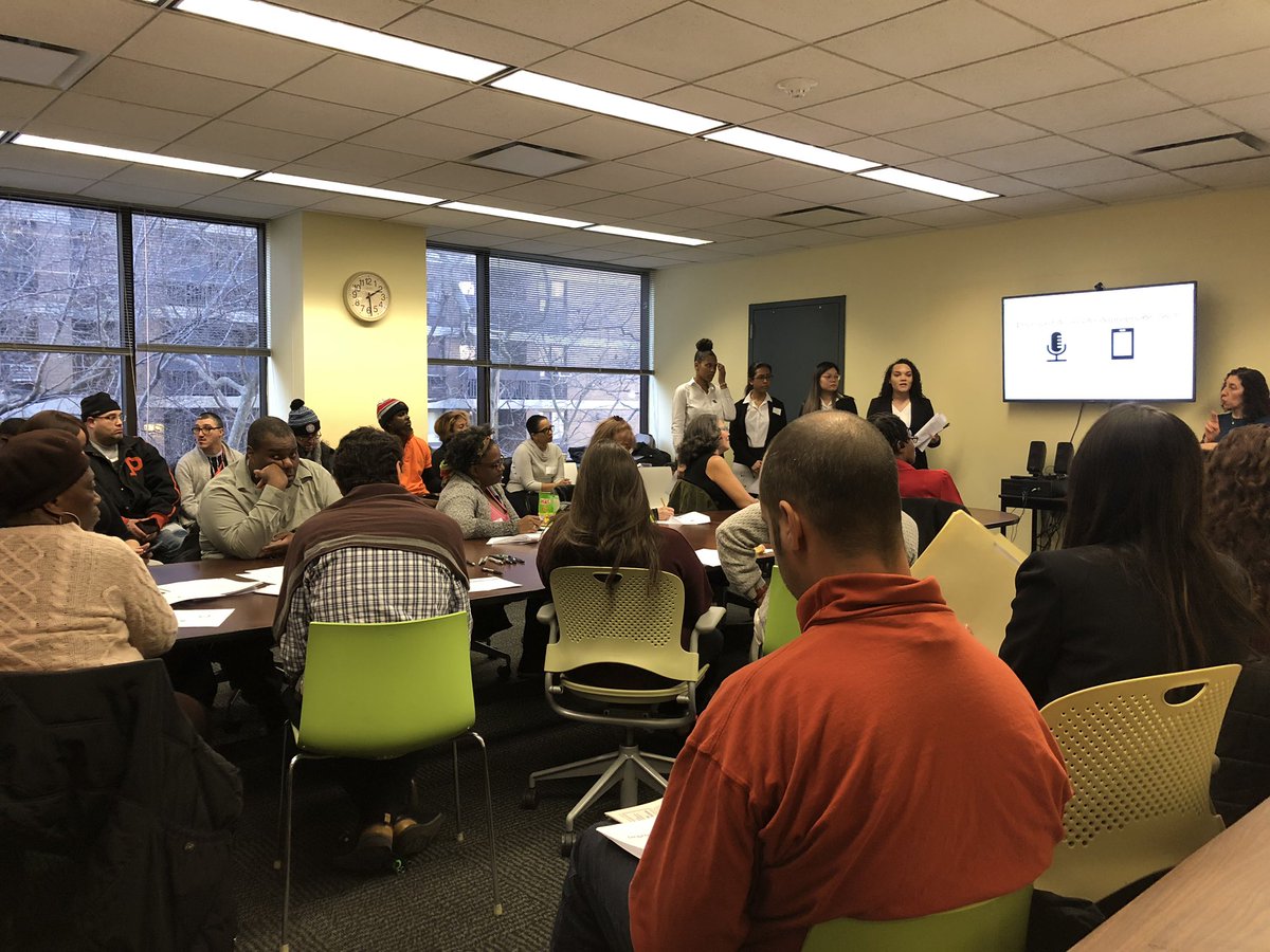 Room full of people with various disabilities sitting in a conference room as four professionally dressed women standing at the front.