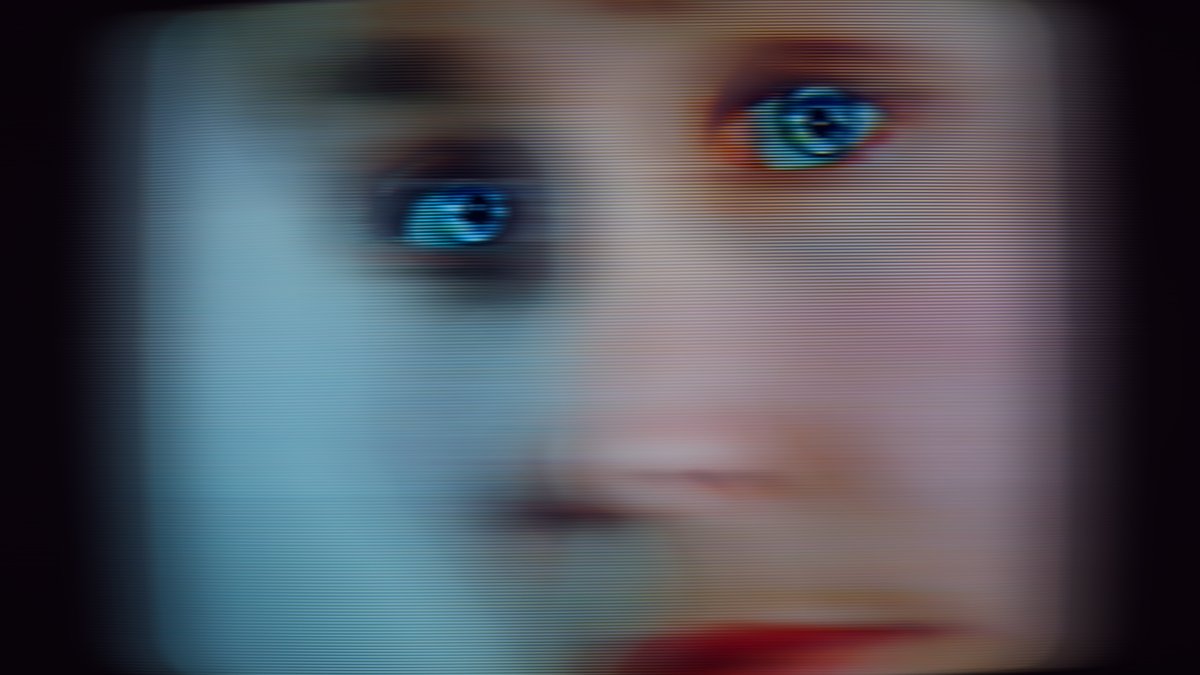 A still from Lynn Hershman Leeson's video work "Seduction of a Cyborg," which depicts a close crop on a white face with blue eyes and red lipstick on a CRT television.