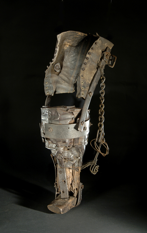 The color photo shows a rusty prosthetic against a black background