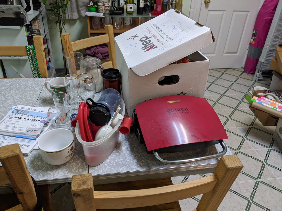 A cardboard box of dishes, a George Foreman grill, and about another box worth of other dishes and kitchen things.