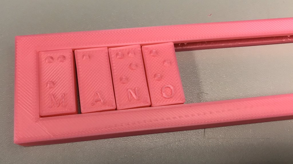 Imagen de cerca de una Regleta o cajetín y unas piezas hechas con la Impresora 3D en donde en cada ficha tocamos la letra y tocamos los puntos que representa. Quedan muy chulas porque están impresos con un filamento de color rosa chicle