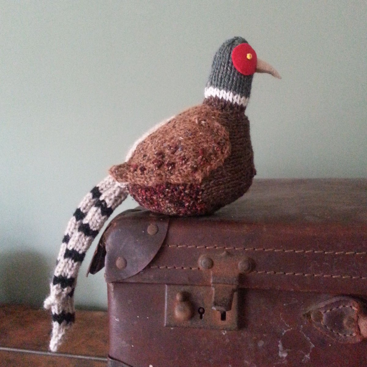 knitted pheasant sitting on top of a suitcase
