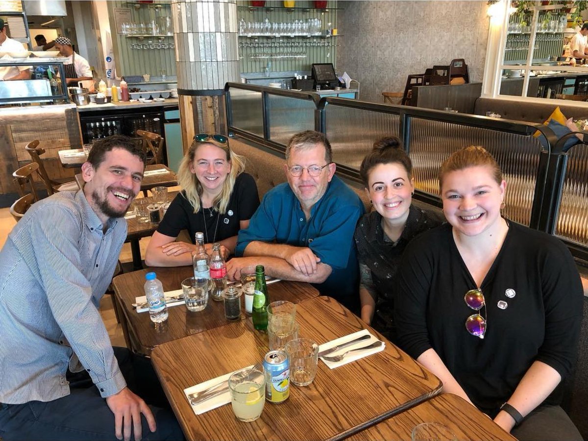 five white people sit around a restaurant table smiling at the camera
