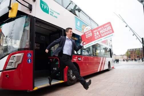 Photo of a man hopping off the 220 bus with a sign that reads “Ireland’s first 24 hour city service”