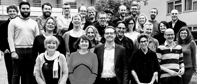 A black and white photo of a group of smiling people standing outside