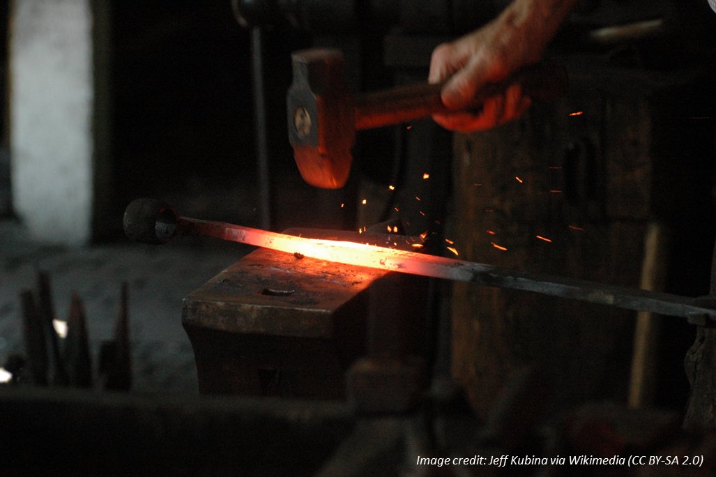 A blacksmith (out of frame except for hands) hammers a piece of glowing hot metal on an anvil. Image credit: Jeff Kubina via Wikimedia Commons)