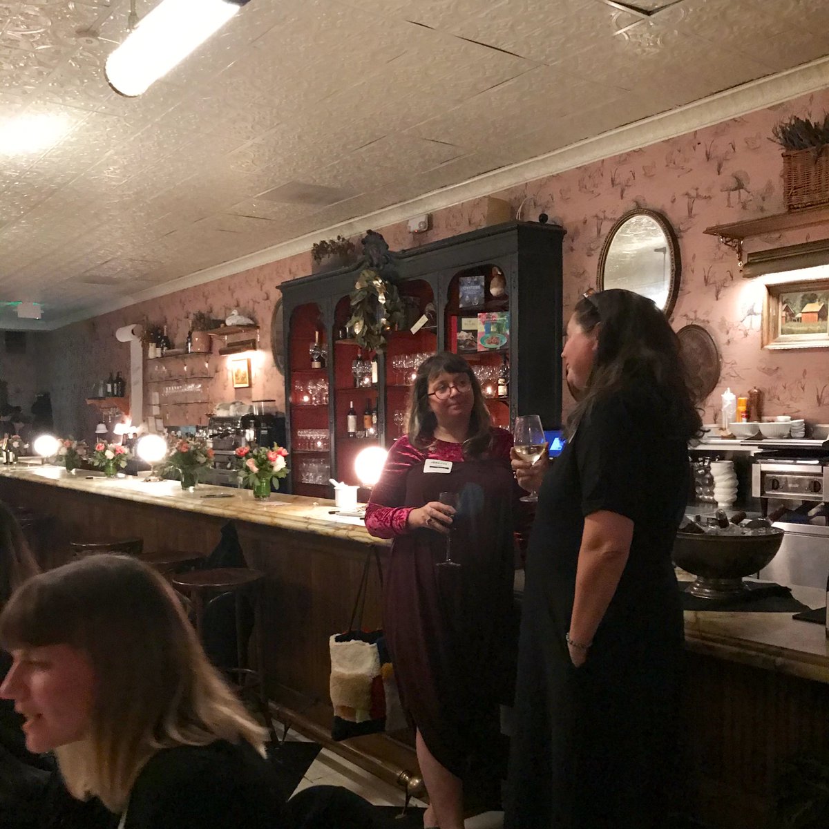 Two women talk design speakers standing by the bar talking at speaker dinner
