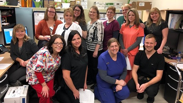 Group of people most in hospital scrubs of various colors all posing and smiling toward the camera.
