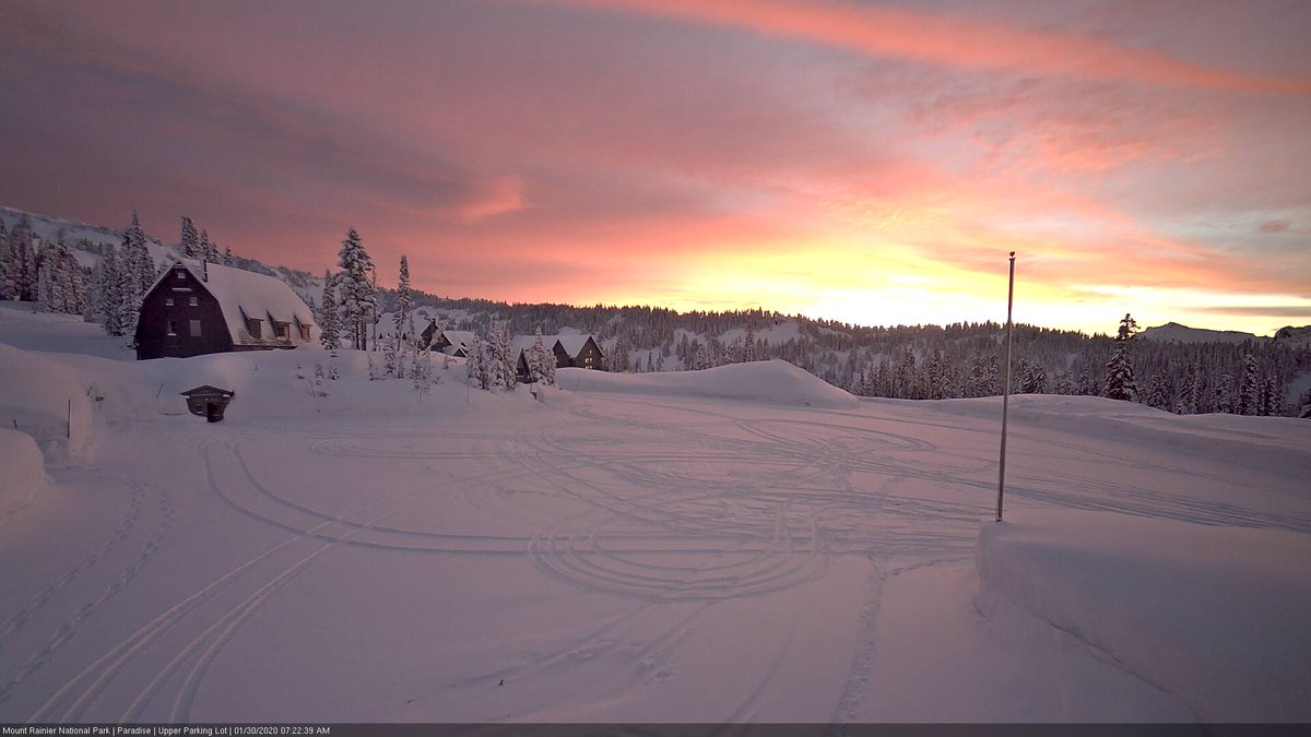 A pink and orange sunrise lights up a snowy parking lot. 
