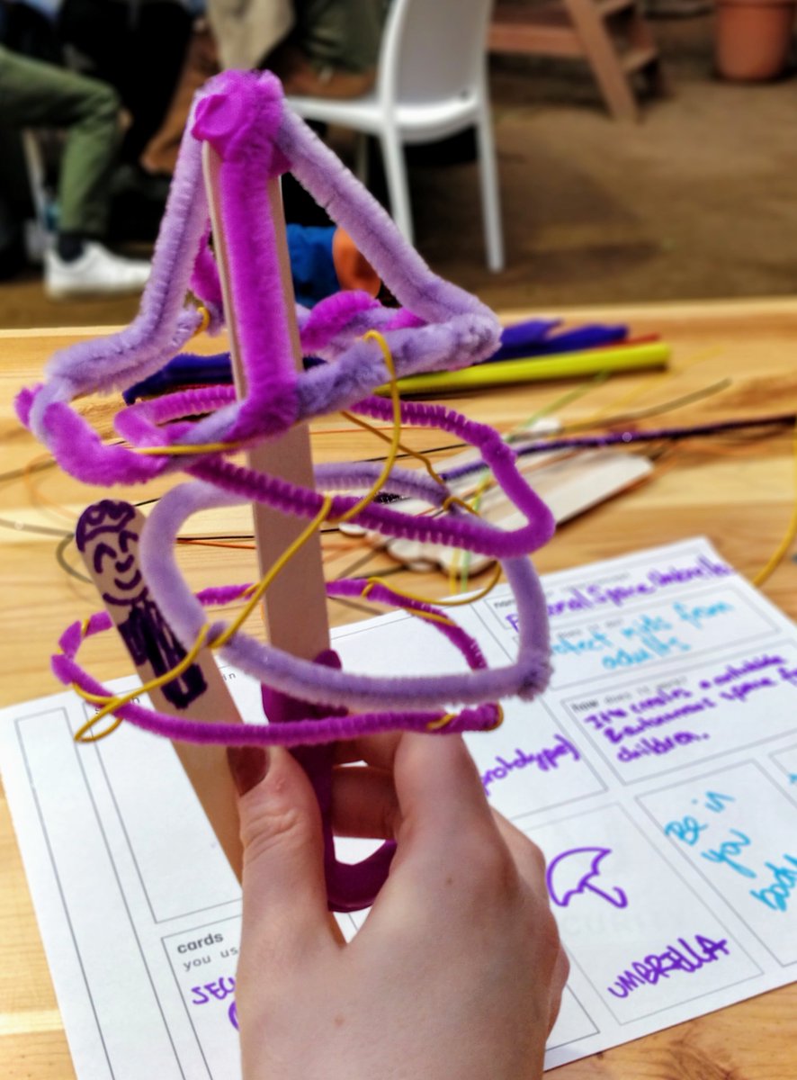 A wobbly futuristic umbrella made of pipe cleaners, play-doh and lollipop sticks protecting a person inside an autonomously controlled personal space.