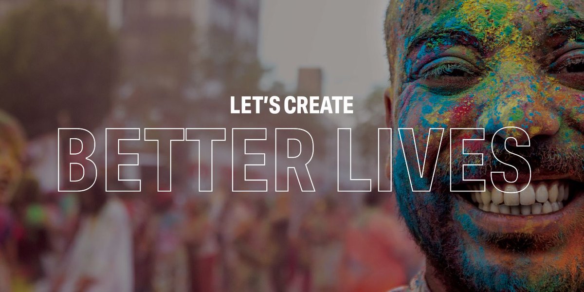 A man is looking directly into the camera smiling. He is covered in paint lots of brightly coloured paint powder. There is text over the image. It says Let's Create Better Lives.