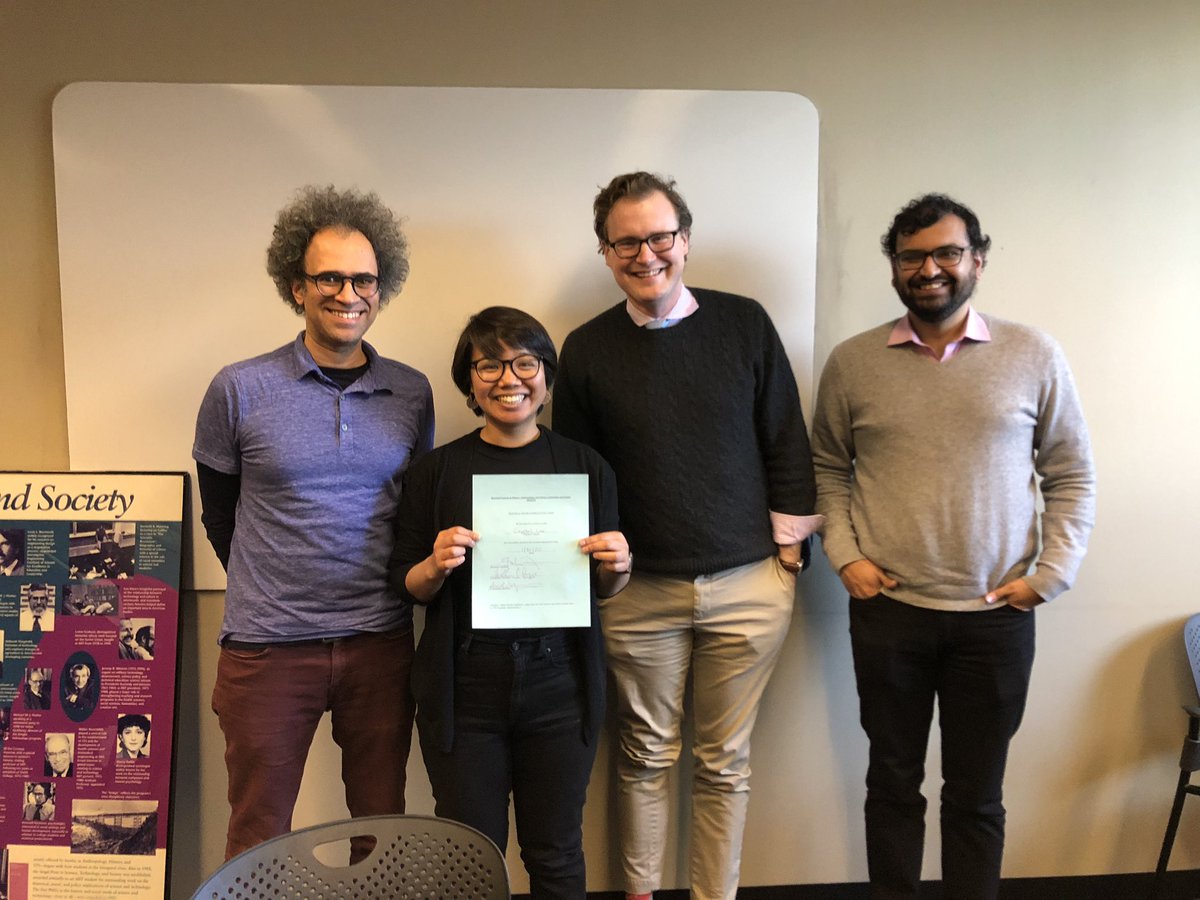 A short haired & short in stature Asian woman with glasses using a paper with lots of signatures, a black man with glasses and curly hair (Graham Jones), a tall white guy with glasses and a collared shirt (Will Deringer), and an Indian man in a gray sweater and glasses (Arvind Satyanarayan)