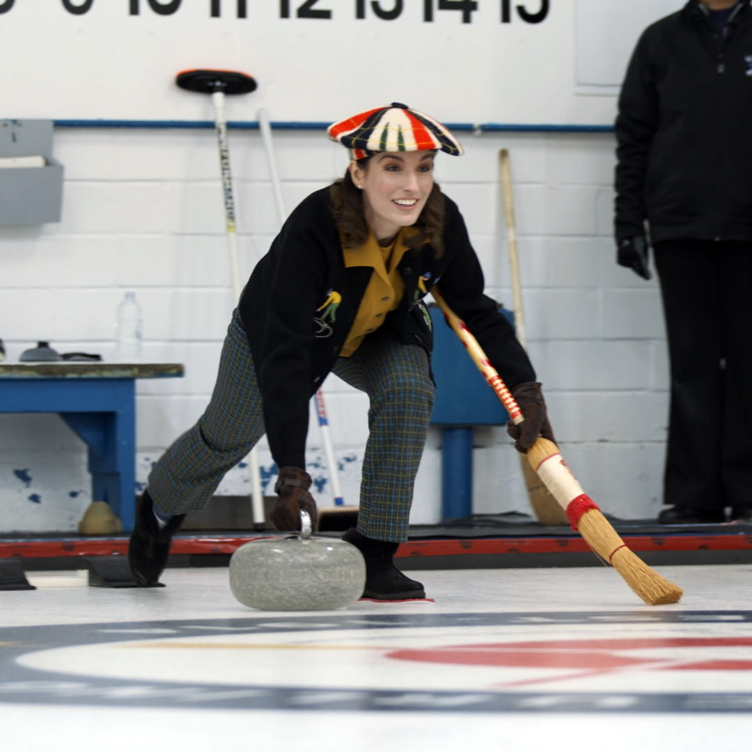 A woman plays curling in 1970s' outfit and equipment.