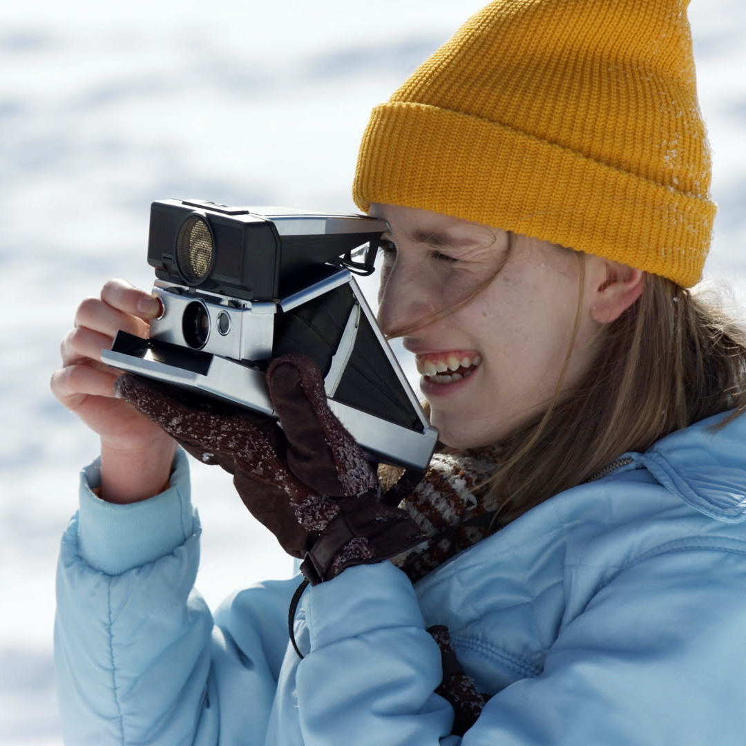 A teenage girl using a Polaroid camera outdoors