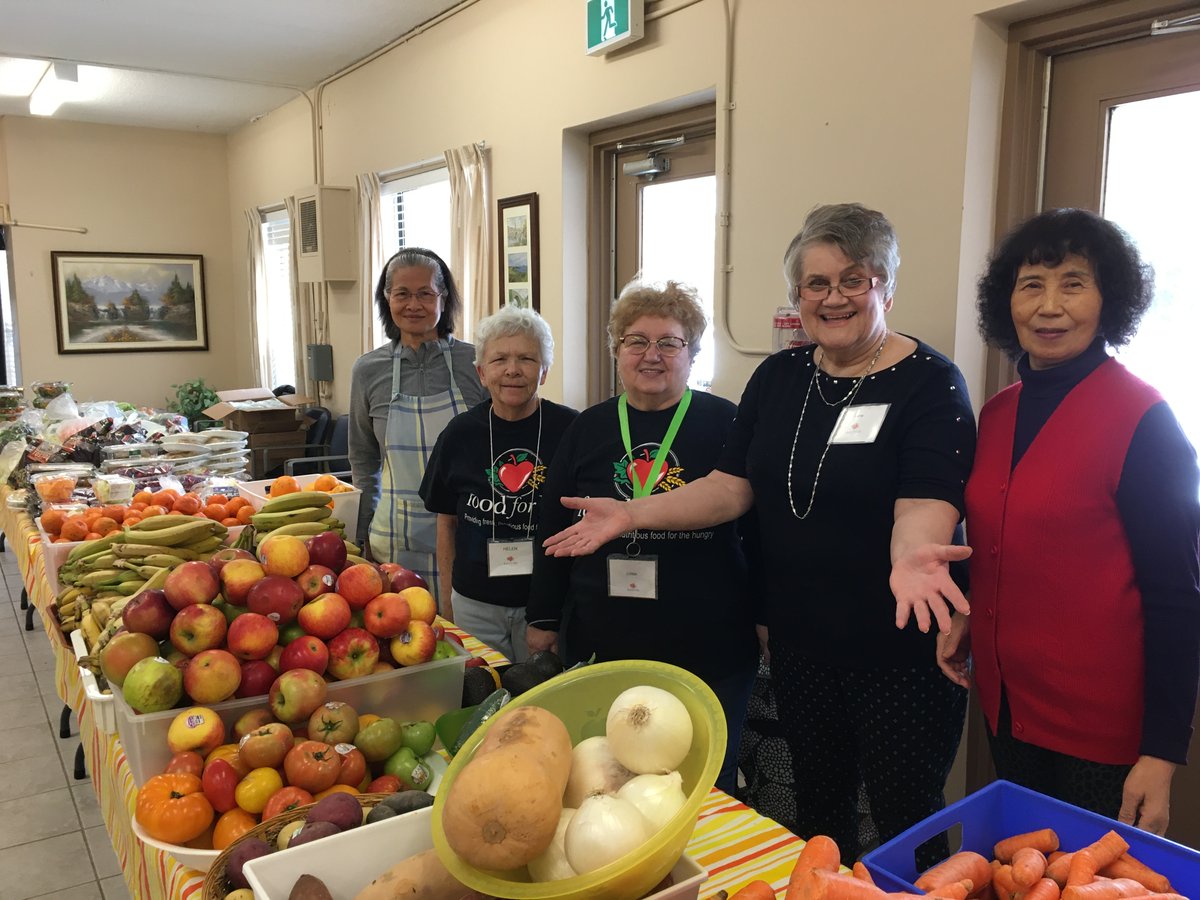 5 people looking at the camera and standing behind tables with a variety of fresh produce on them.
