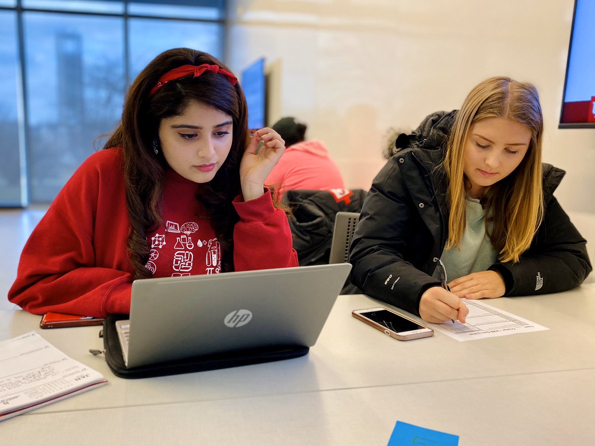 Two students working at a table with a laptop and paper