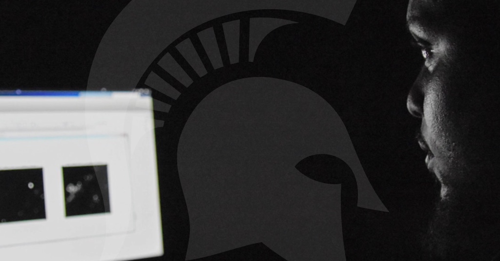 Close-up photo of a student's face looking at a computer in darkness with the computer screen glowing