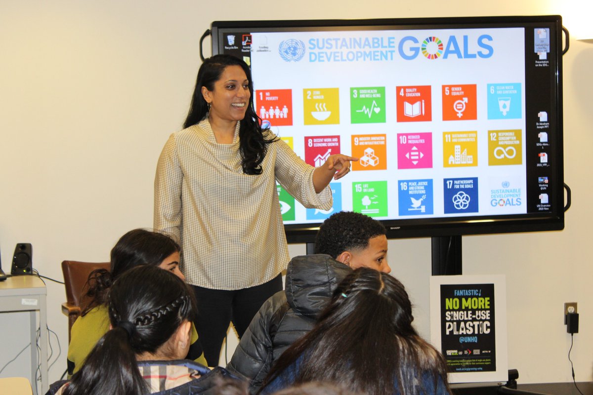 Commissioner Abeywardena speaks in front of the class, in front of a screen with the Sustainable Development Goals symbols.