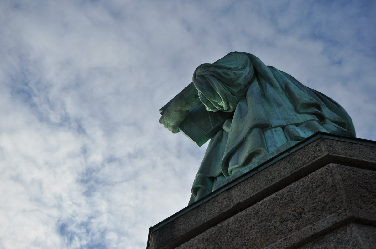Looking up at the statue from the top of the pedestal. The lower right corner has the stone pedestal and the bottom of the statue's tablet can be seen in the robed arm.