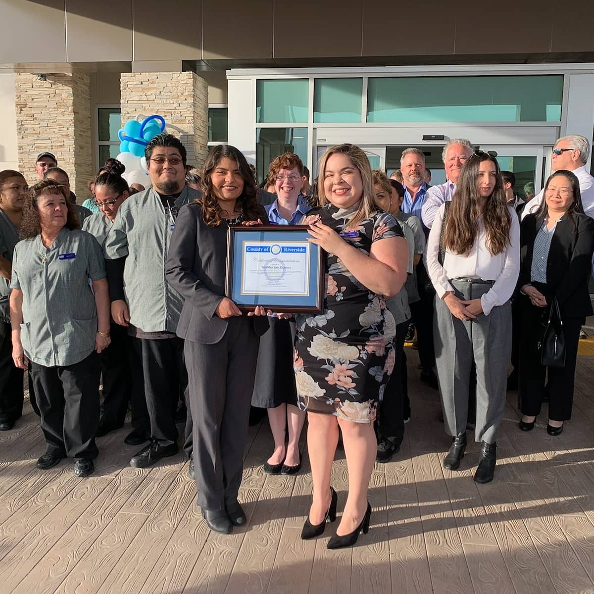 Sarah Rodriguez presenting a framed certificate to another person in front of a crowd of people.