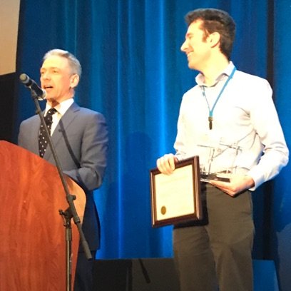 Andrei Iancu speaking at podium and man standing next to him holding award