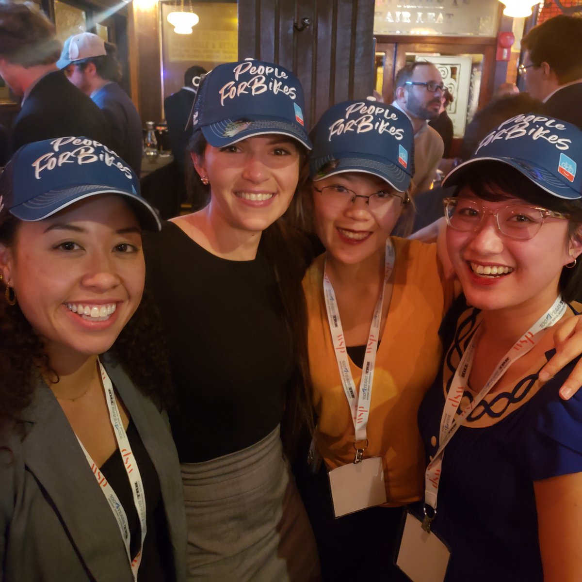 A diverse group of four female college students smiling and wearing PeopleForBikes hats