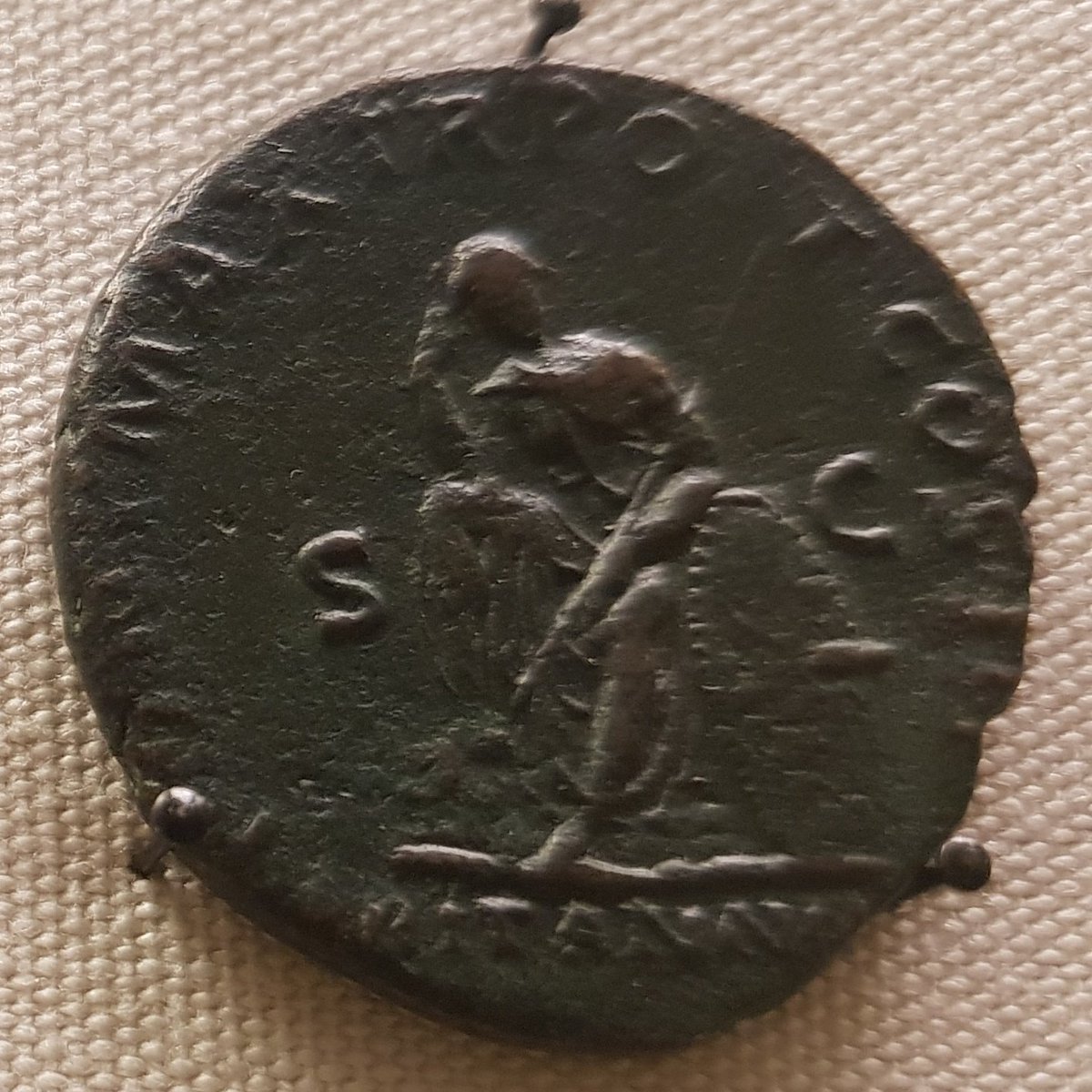 The reverse of an 'as' (low denomination Roman coin), showing a slumped seated female figure, head resting on one hand, holding a spear, with a shield by her side. Underneath her is the name Britannia