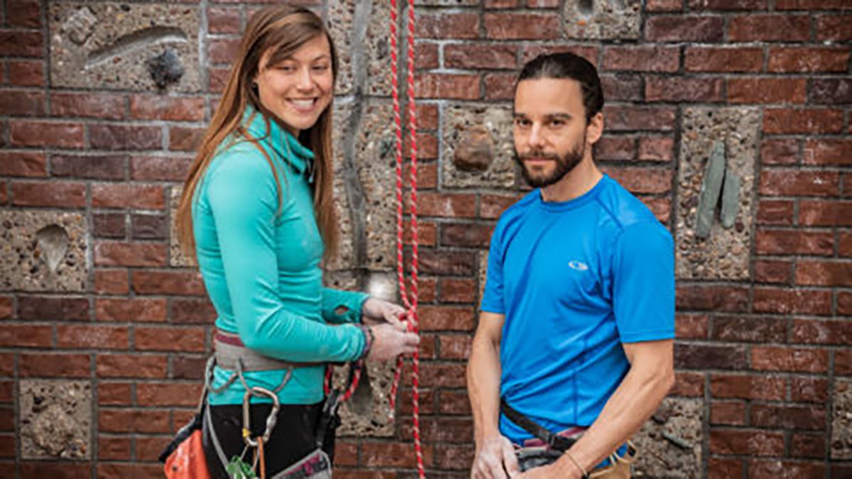 Drew Wilkinson and Holly Beale posing for a photo while standing in front of a climbing wall. 