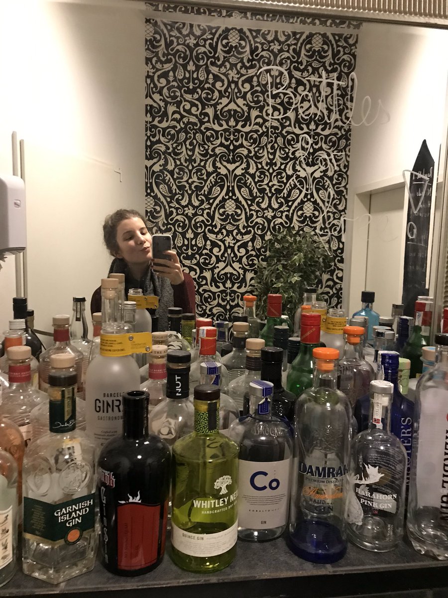 Mirror selfie with many, many empty gin bottles on the counter.