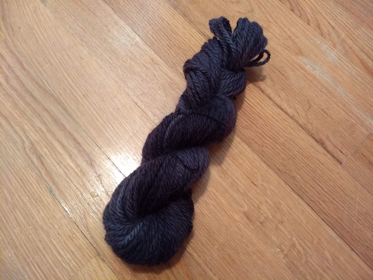A skein of handspun yarn, neatly twisted back on itself. It is spun as a fairly consistent 2-ply yarn, on the edge of worsted and bulky, and is dyed in a range of dark greys bordering on black.
