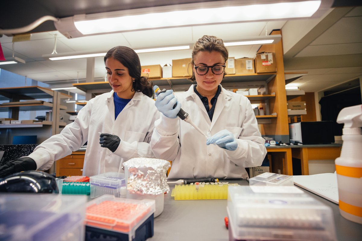 Two students in white lab coats conduct research.