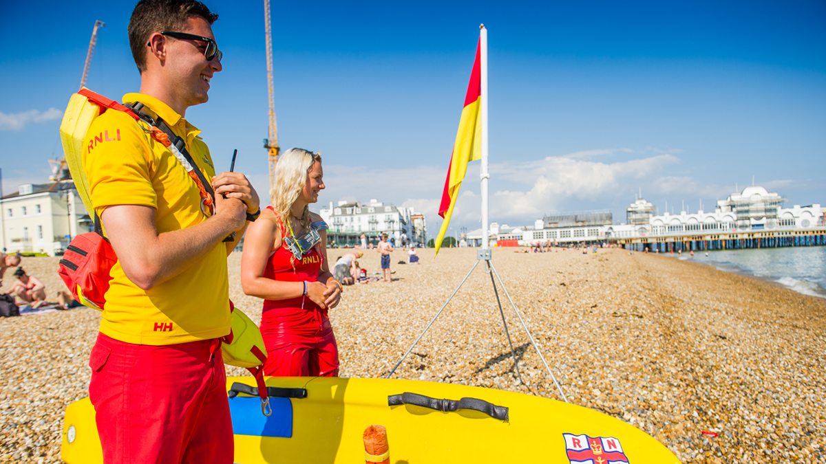 A male and female lifeguard on a sunny day at the beach smiling and looking out to sea