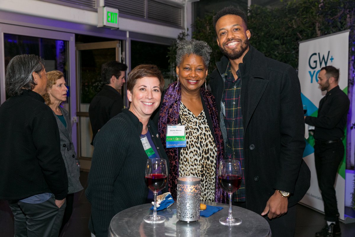 two women and a man standing by table smiling
